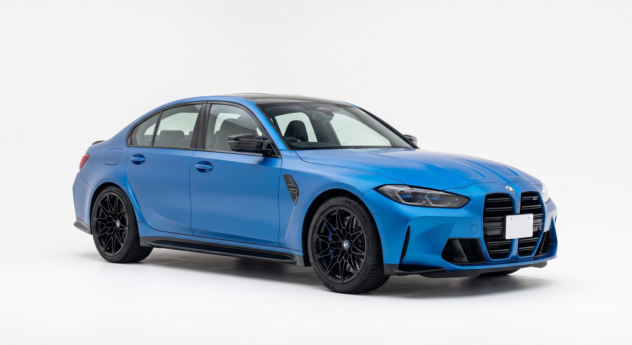 白い背景スタジオに置かれた、マットブルー（艶消し青）のBMW M3スポーツセダン。大きな縦型キドニーグリルと黒いアルミホイールが印象的なフロント斜めからの外観写真。