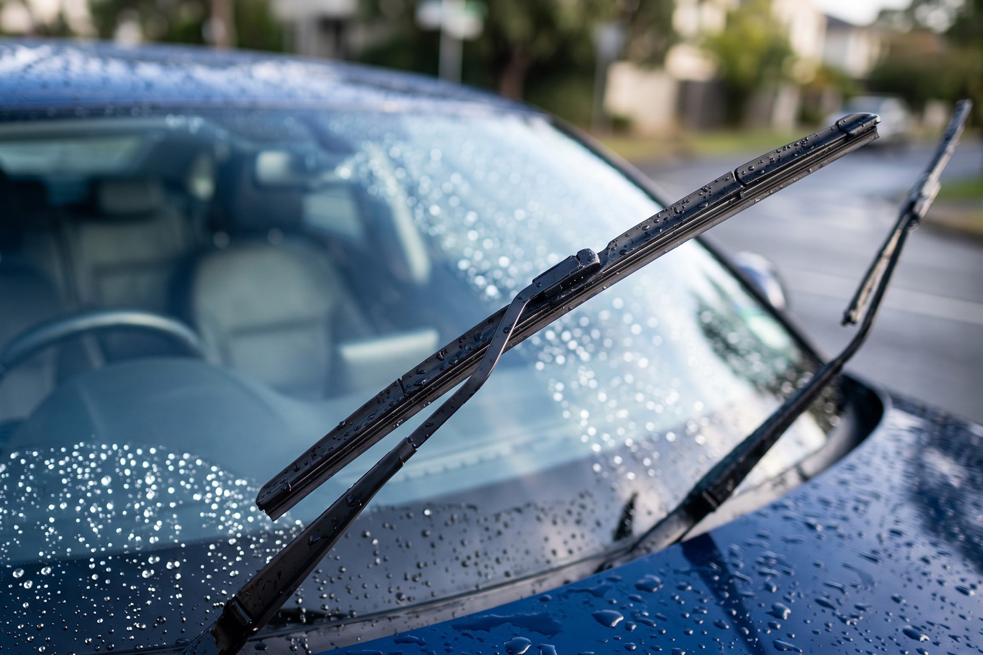 水滴が細かく弾く車のフロントガラスと持ち上げられたワイパーブレード。撥水コーティングの効果や車のガラスメンテナンス風景を表す画像です。